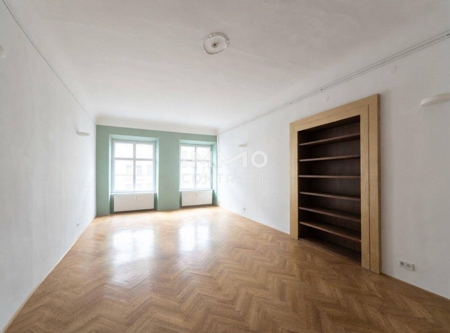 Heller Raum mit Fischgrätparkett, weißen Wänden und einem eingebauten Holzregal.