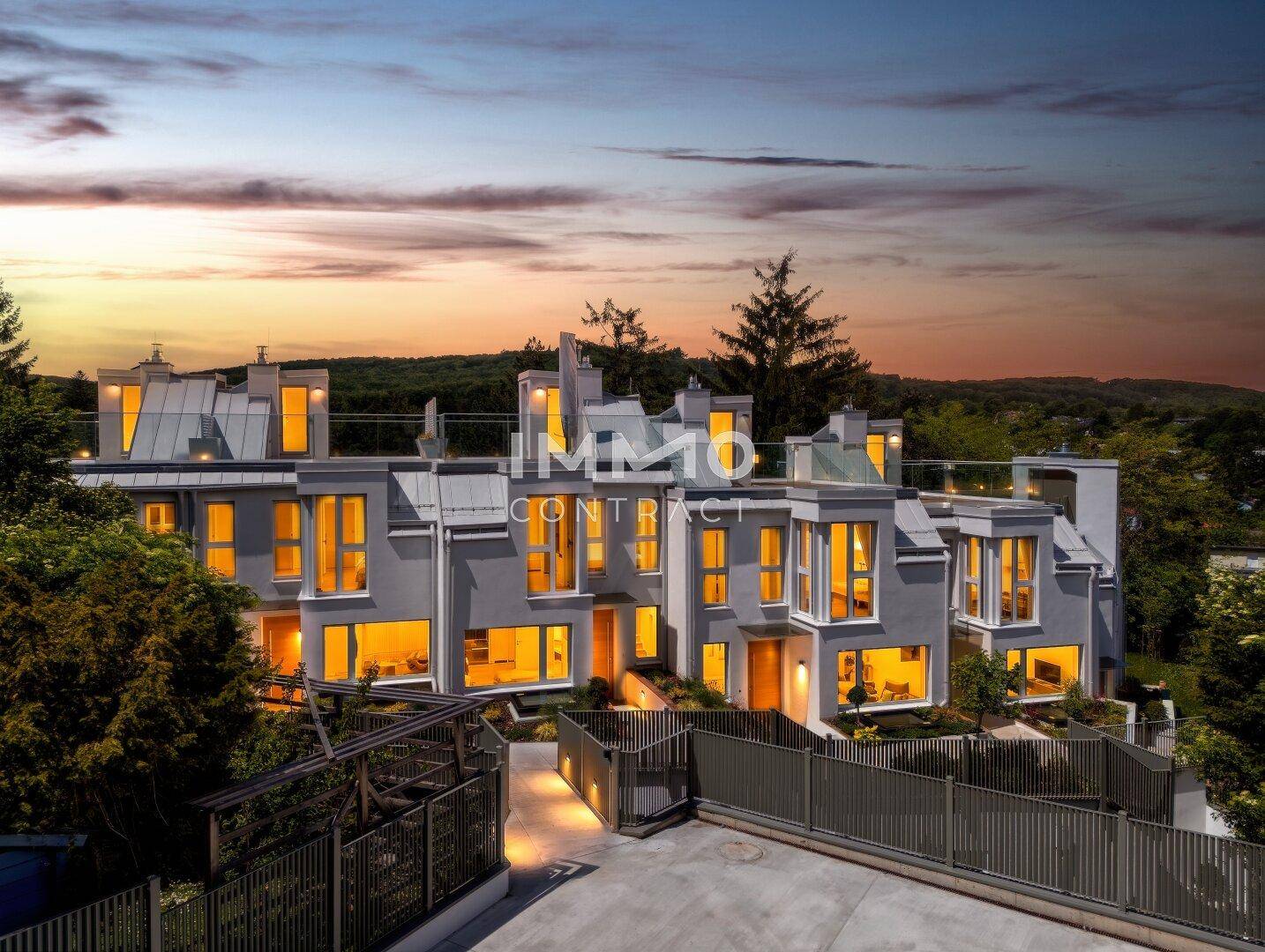 Luftaufnahme eines modernen Wohnkomplexes bei Dämmerung mit beleuchteten Innenräumen und viel Grün.