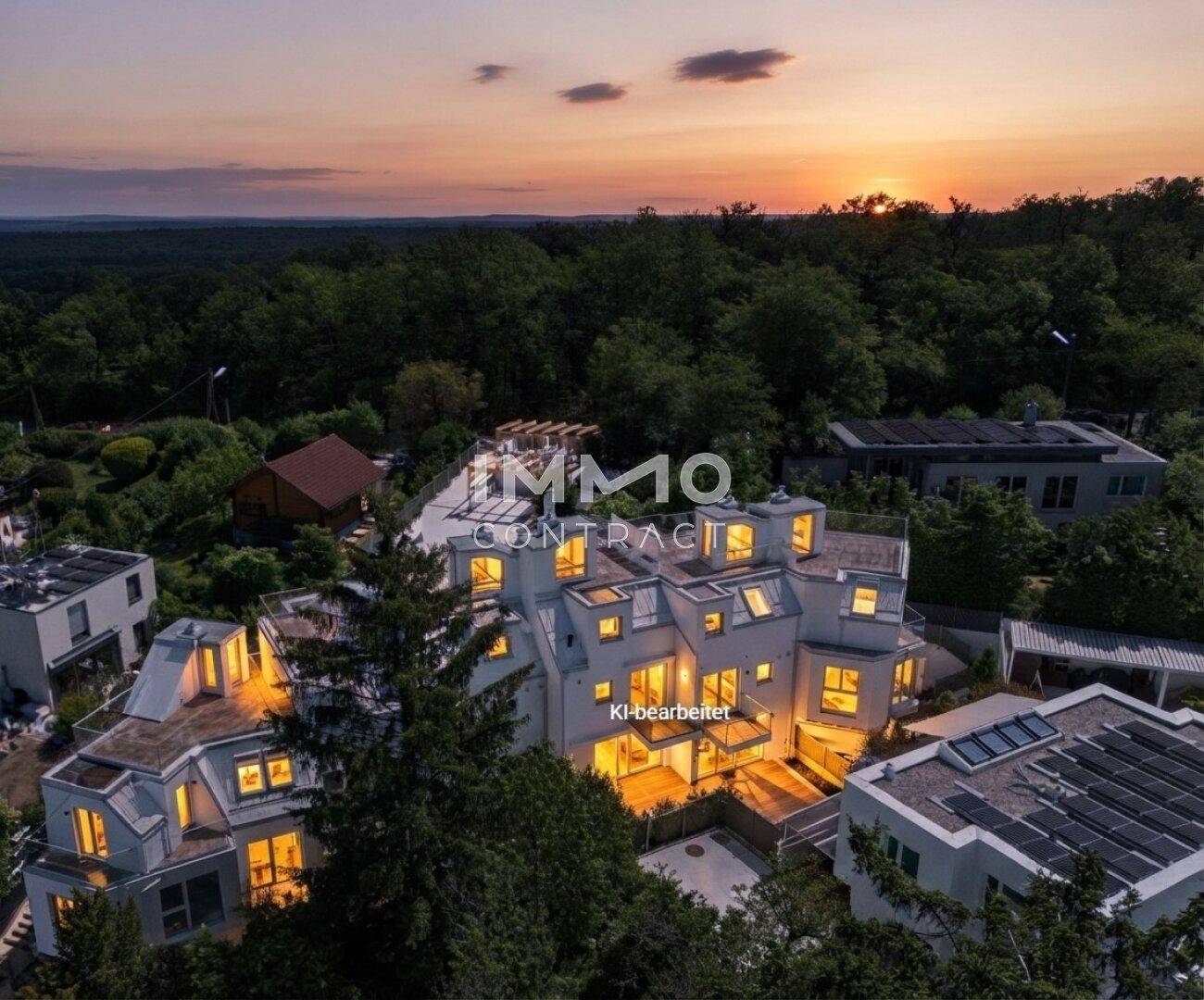 Luftaufnahme eines modernen Wohnkomplexes bei Sonnenuntergang, umgeben von Bäumen und Hügeln.