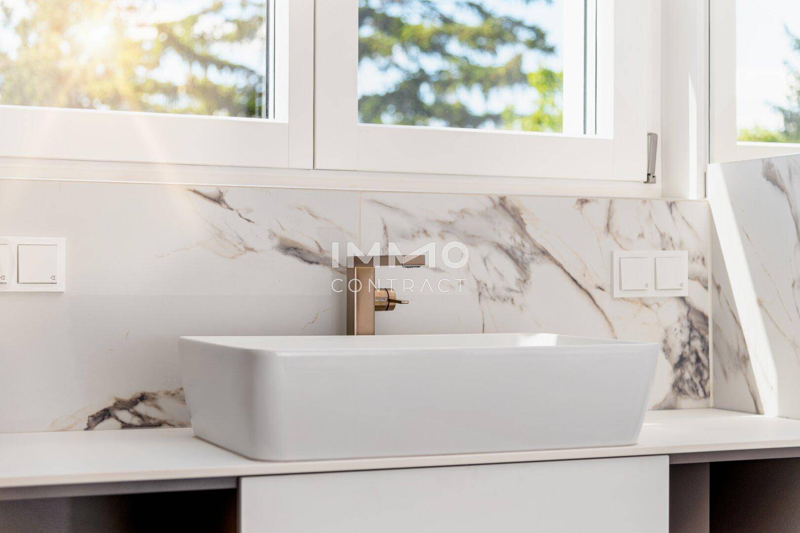 Modernes Badezimmer mit Aufsatzwaschbecken, goldfarbenem Wasserhahn und Marmoroptik-Fliesen.