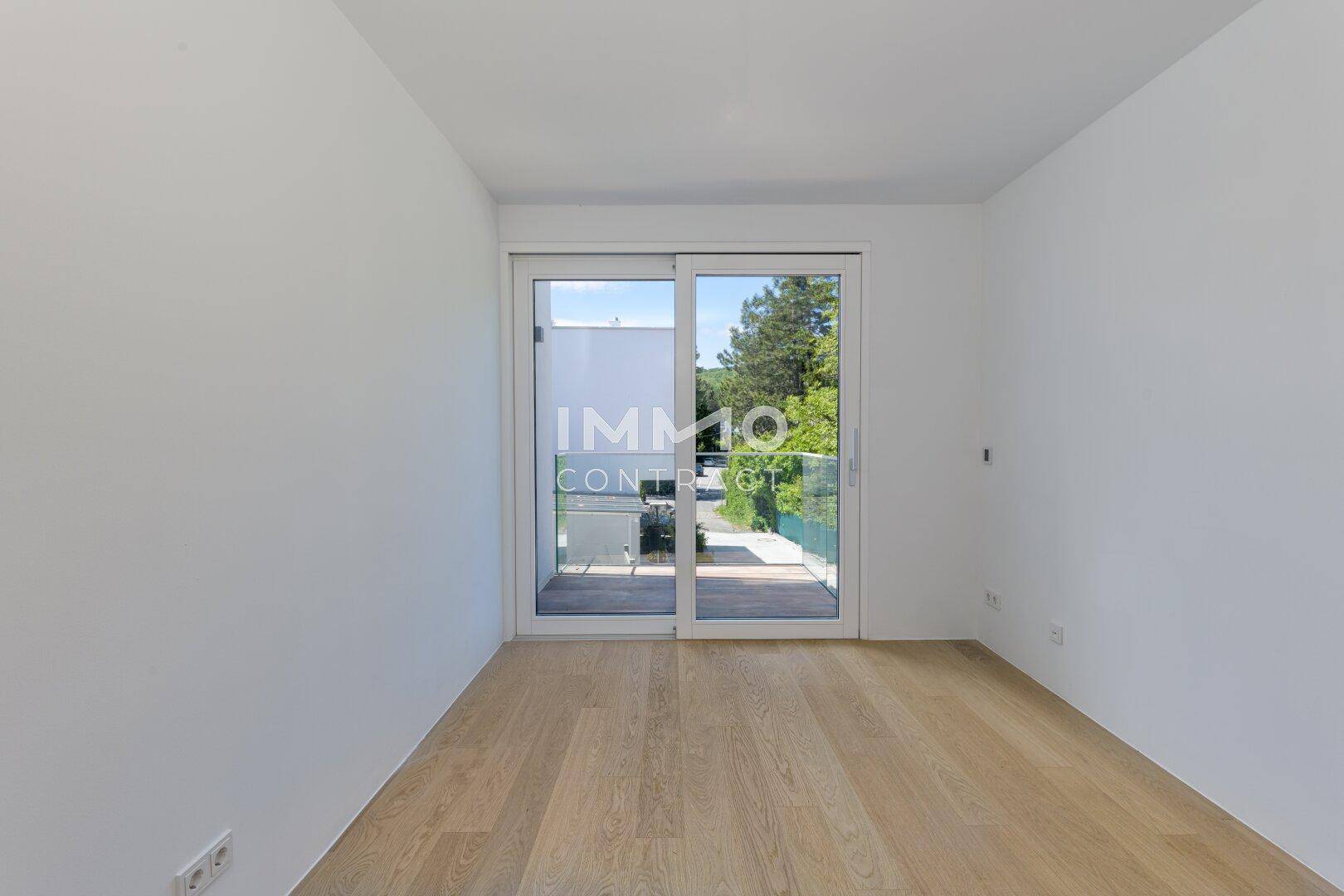 Helles Schlafzimmer mit Holzboden und Zugang zu einem Balkon durch eine Glasschiebetür.