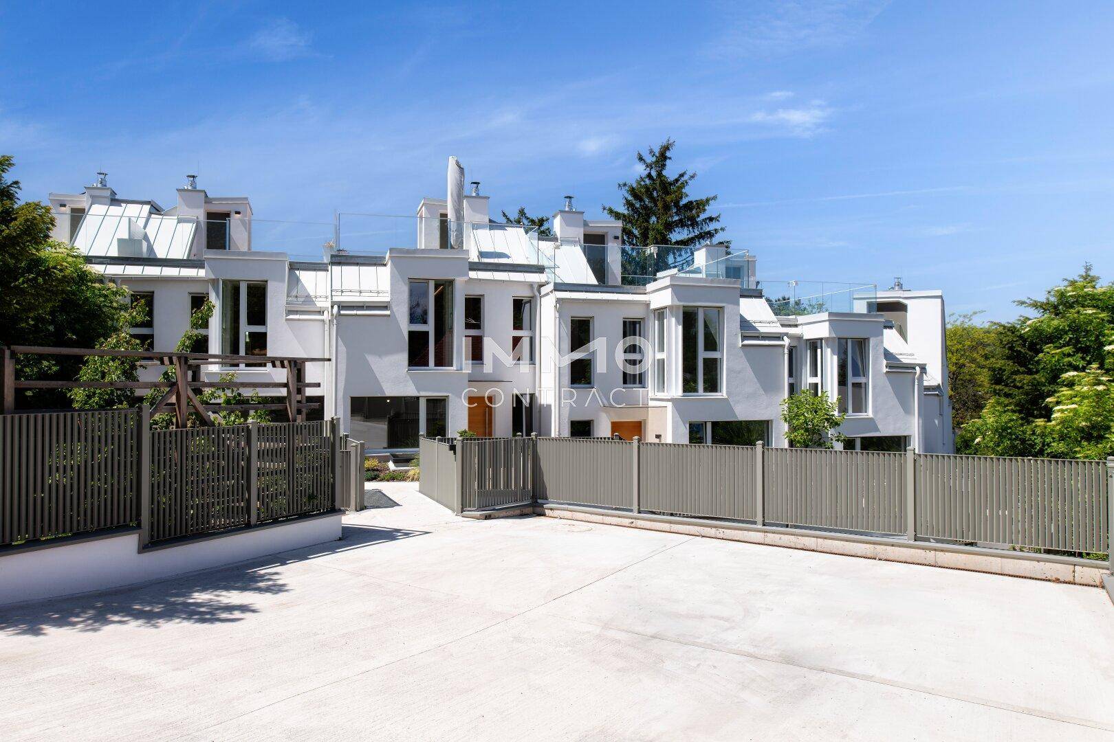 Moderne Reihenhäuser mit weißer Fassade, großen Fenstern und einem gemeinsamen Vorplatz.