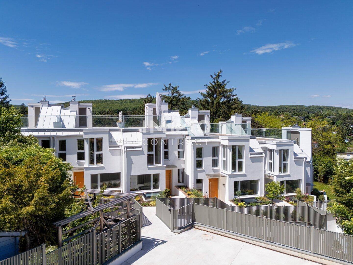 Moderne Wohnanlage mit weißer Fassade, großen Fenstern und Terrassen in grüner Umgebung.