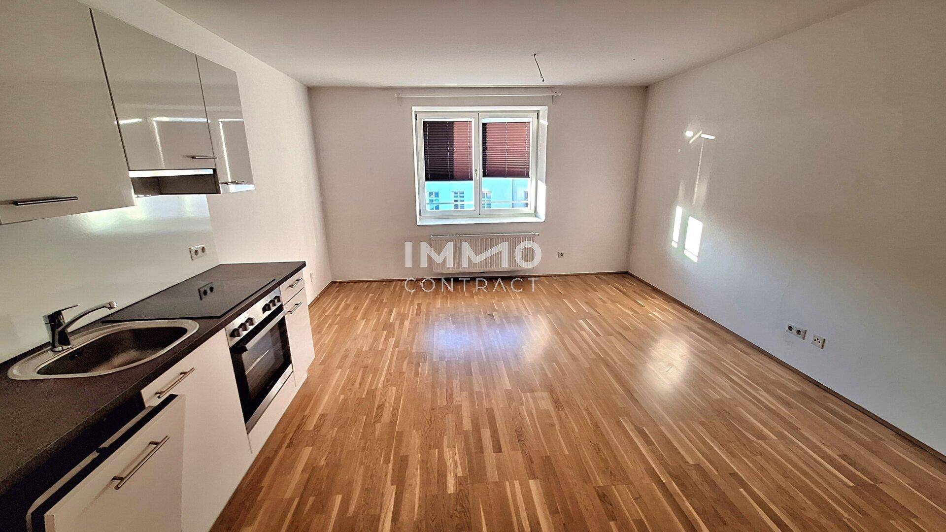 Heller, leerer Wohnraum mit integrierter Küchenzeile und Fenster, ideal für ein Studio-Apartment.