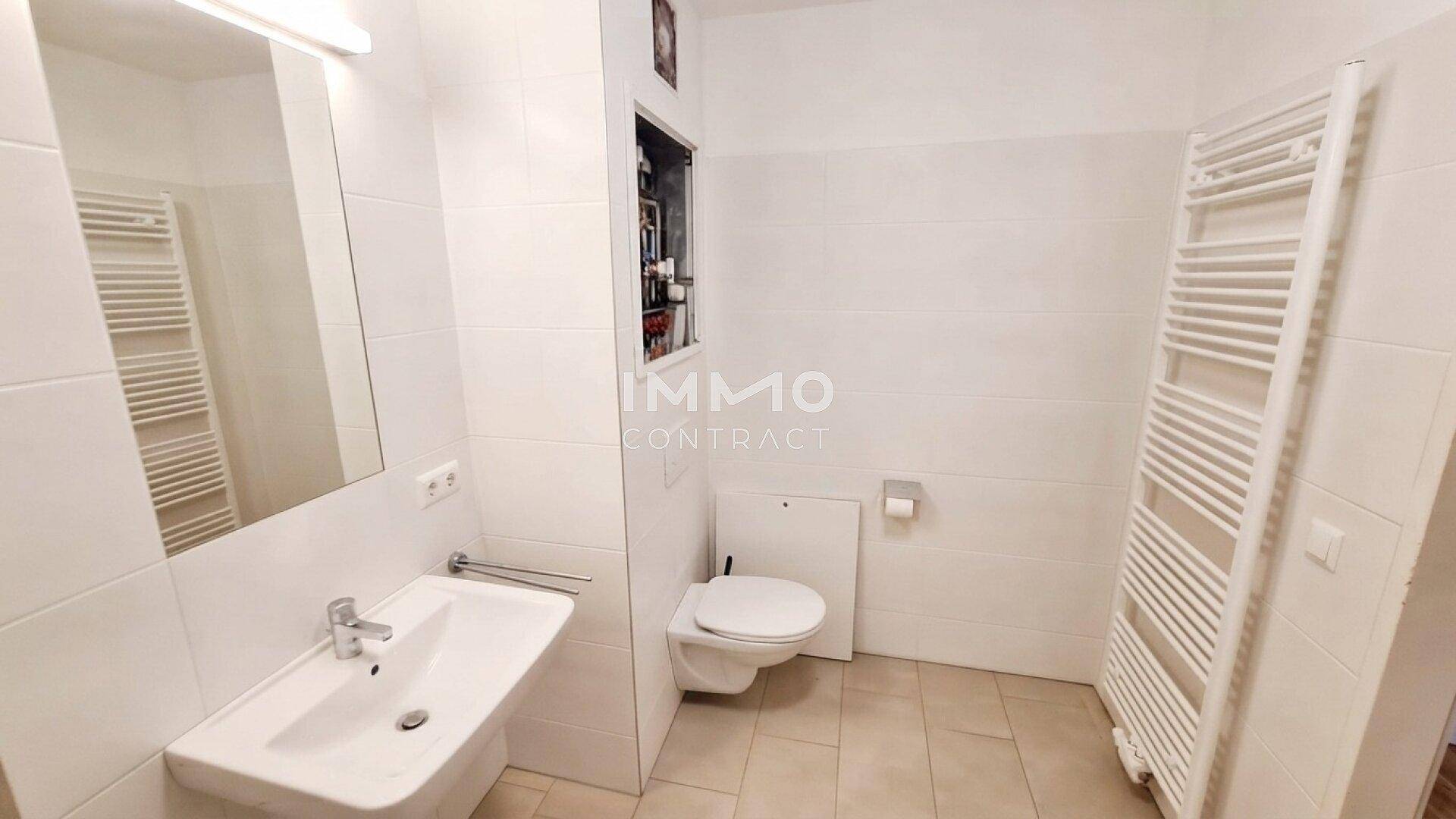 Modernes Badezimmer mit Wand-WC, Waschbecken und beheiztem Handtuchhalter, hell gefliest.