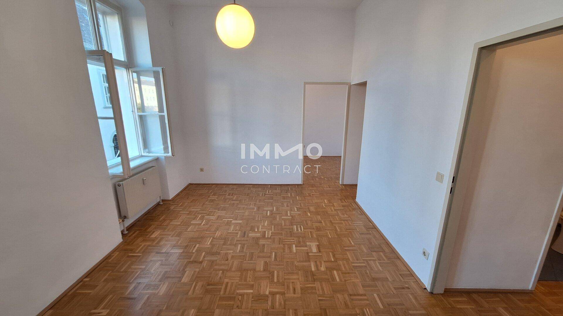 Geräumiger, leerer Raum mit Parkettboden und hohen Fenstern, ideal für Wohnzwecke.