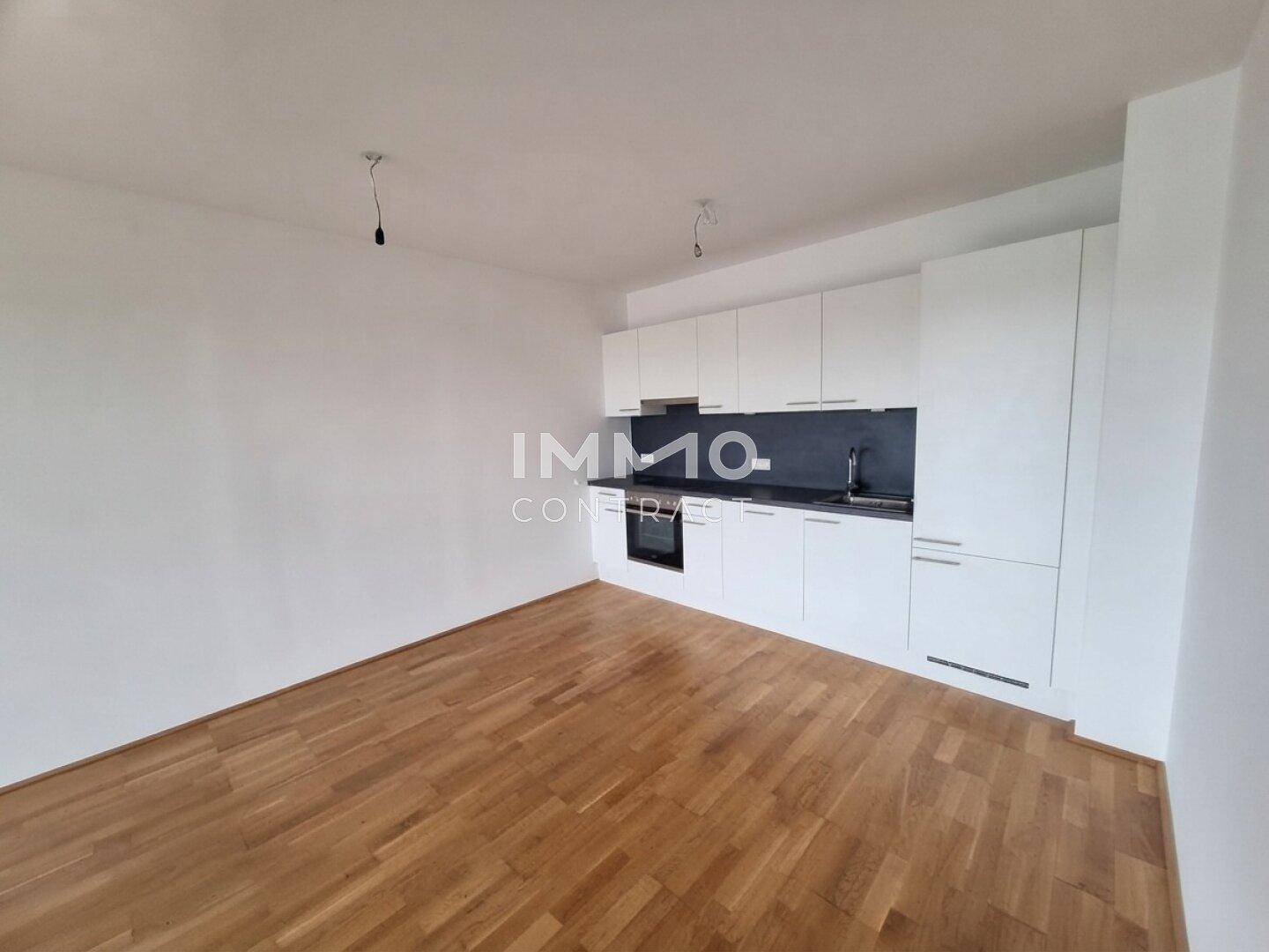 Moderne Einbauküche mit weißen Schränken und dunkler Arbeitsplatte in einem offenen Wohnbereich mit Parkettboden.