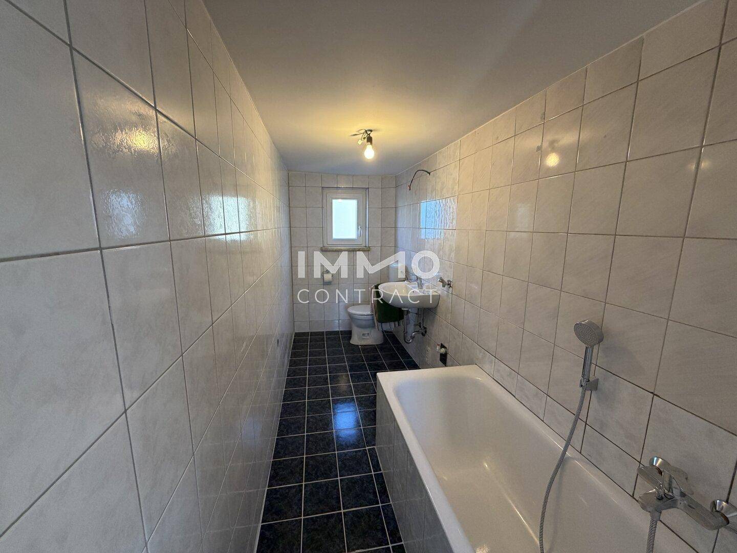 Gefliestes Badezimmer mit Badewanne, Waschbecken und Fenster für natürliche Belüftung.