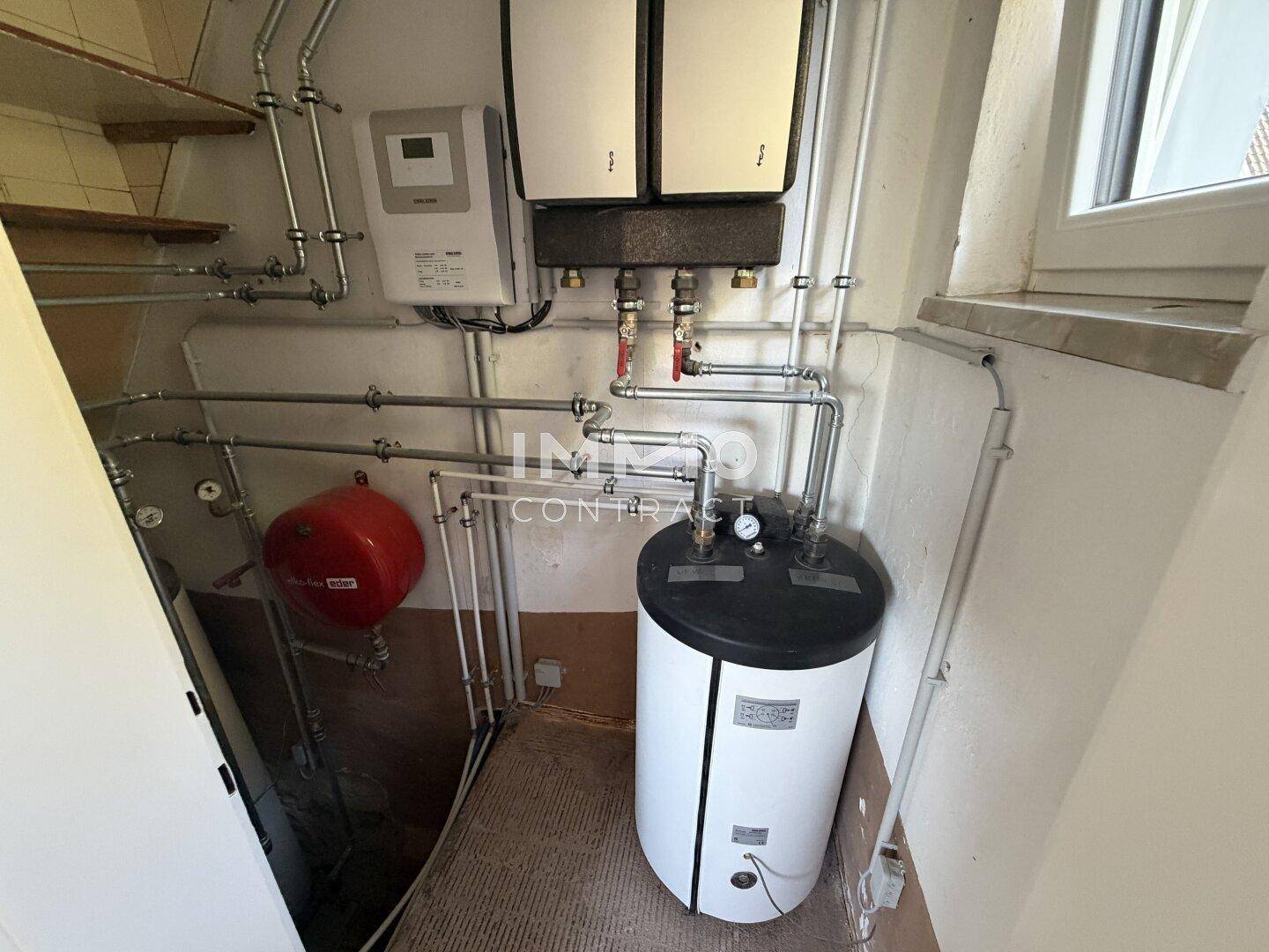 Technikraum mit Heizungsanlage, Warmwasserspeicher und sichtbaren Rohrleitungen.