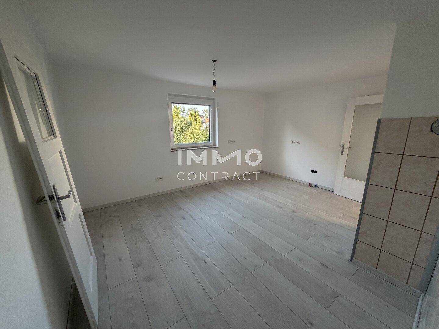 Geräumiges, unmöbliertes Zimmer mit hellem Boden und Fenster, das viel Tageslicht hereinlässt.