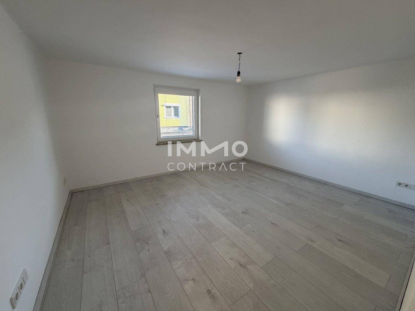 Unmöbliertes Zimmer mit hellem Laminatboden und einem Fenster, das den Raum erhellt.
