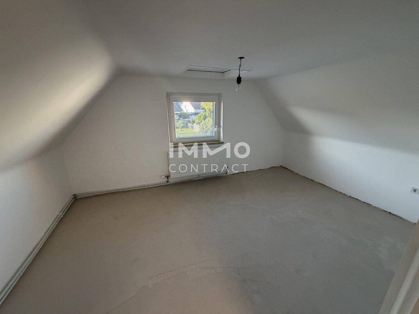 Dachgeschossraum mit schrägen Wänden, Estrichboden und einem kleinen Fenster für Tageslicht.