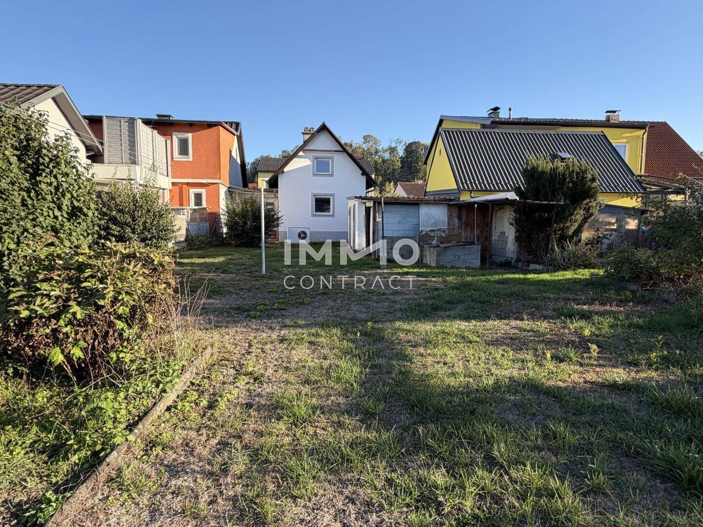 Großer Gartenbereich hinter dem Haus mit Rasenfläche und angrenzenden Nebengebäuden.