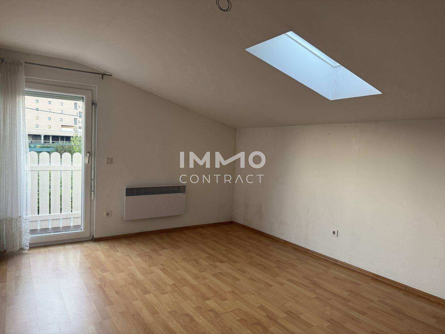 Dachzimmer mit Laminatboden, Dachfenster und Zugang zu einem kleinen Balkon.