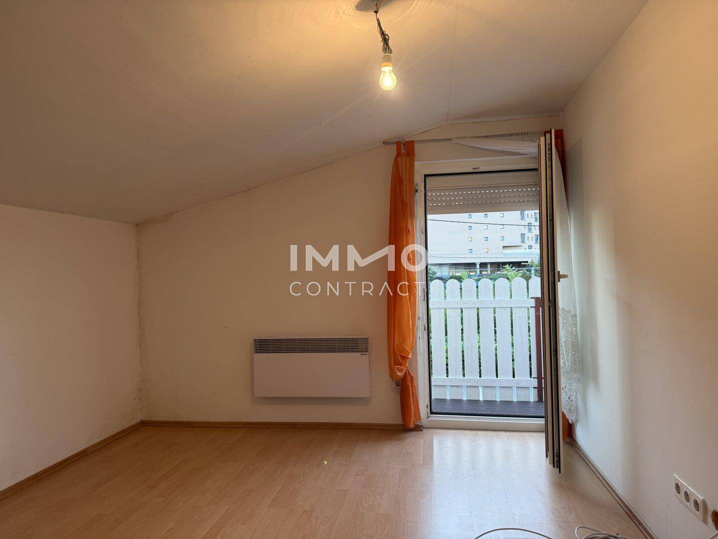 Helles Zimmer mit Laminatboden, Dachschräge und Zugang zu einem kleinen Balkon.
