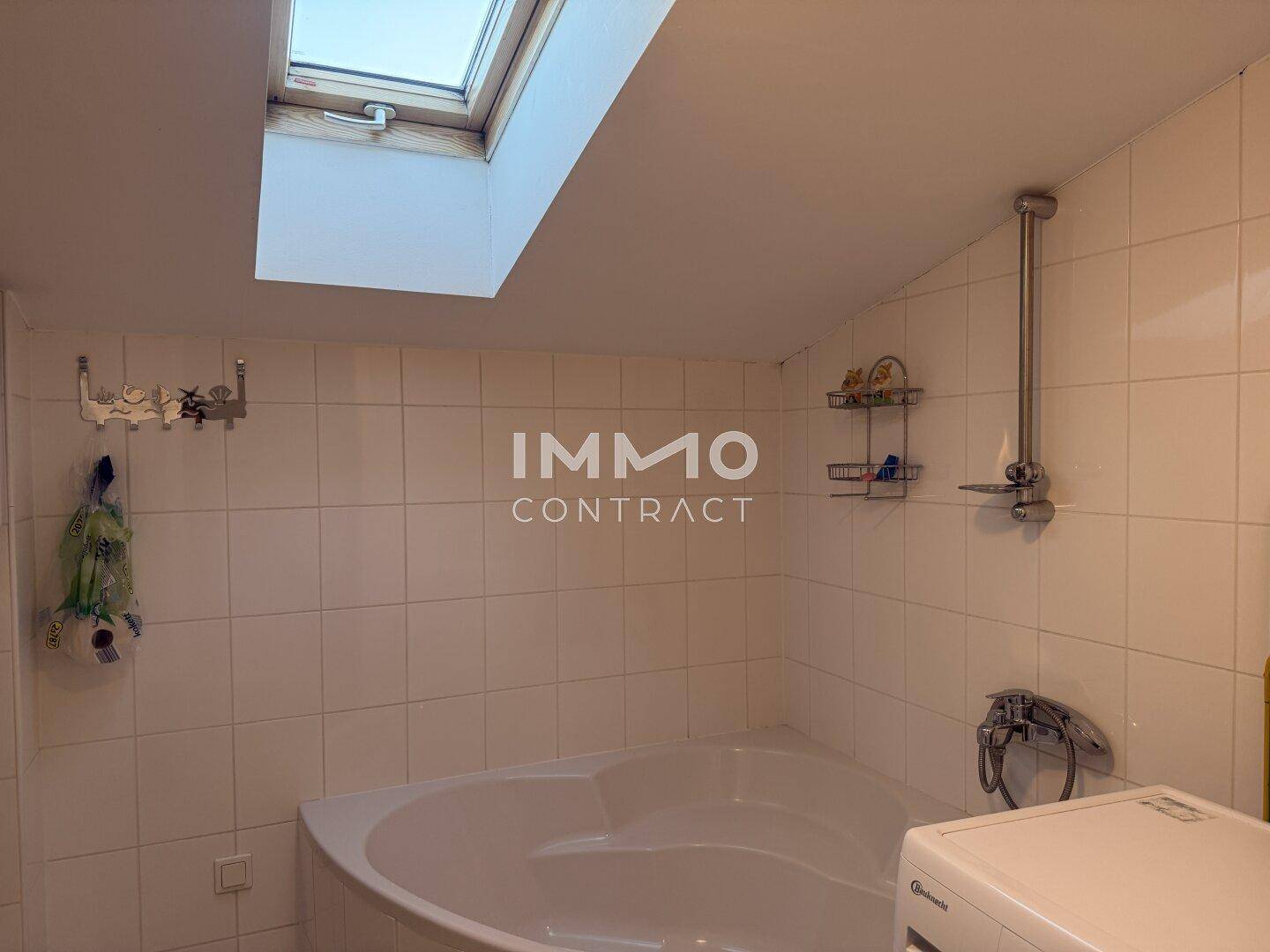 Badezimmer mit Eckbadewanne, weißen Fliesen und einem Dachfenster für Tageslicht.