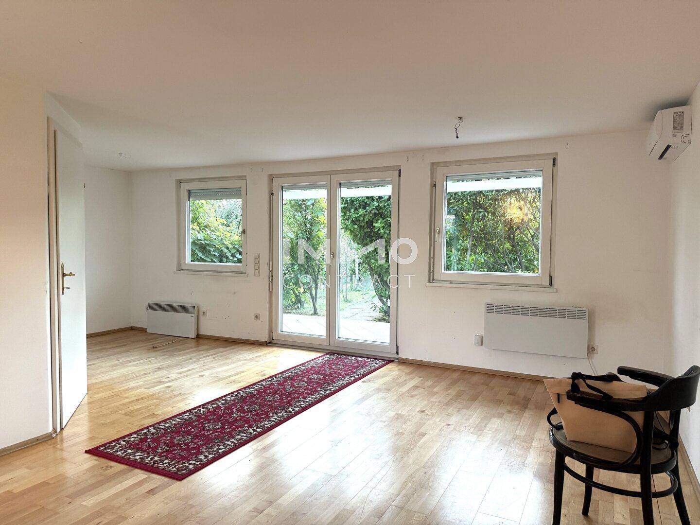 Helles Wohnzimmer mit Holzboden, großen Fenstern und Zugang zum Außenbereich.