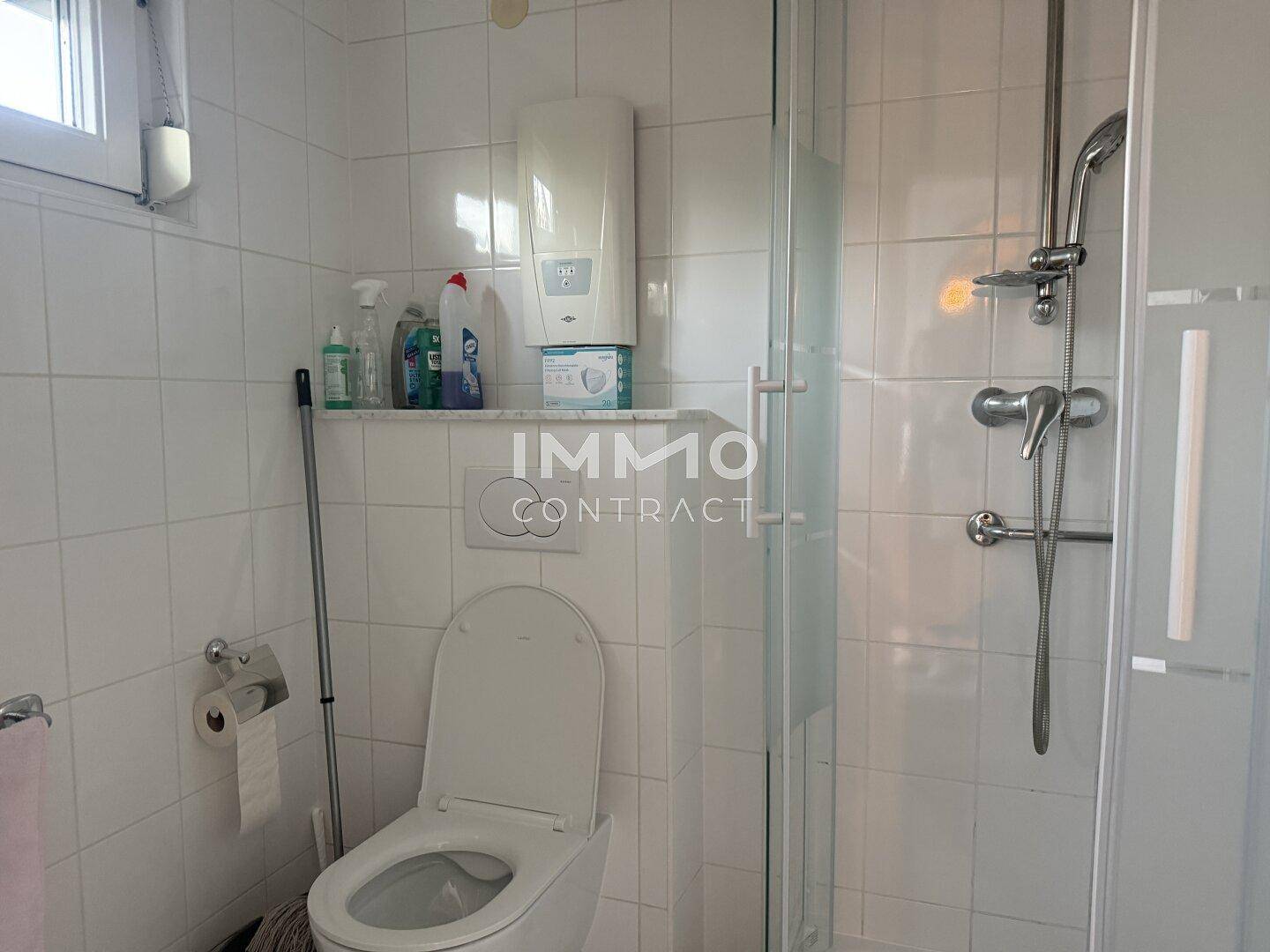 Gefliestes Badezimmer mit Toilette, Duschkabine und Fenster für natürliche Belüftung.
