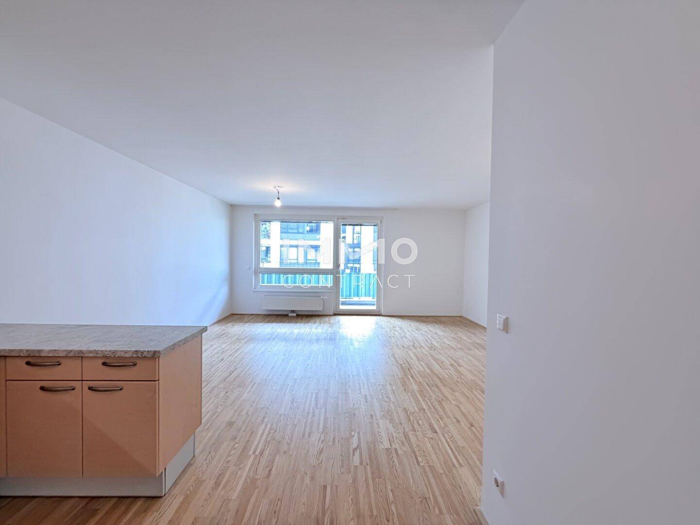 Geräumiges Wohnzimmer mit hellem Parkettboden und Zugang zu einem Balkon.