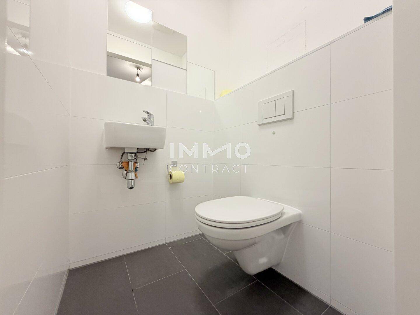 Funktionelles Gäste-WC mit wandhängender Toilette und kleinem Waschbecken, modern gefliest.