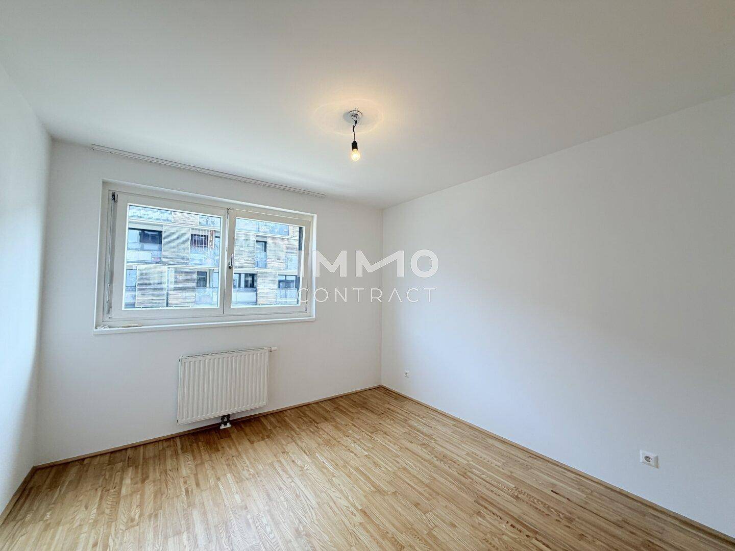 Helles Schlafzimmer mit Parkettboden und großem Fenster, bereit zur individuellen Gestaltung.