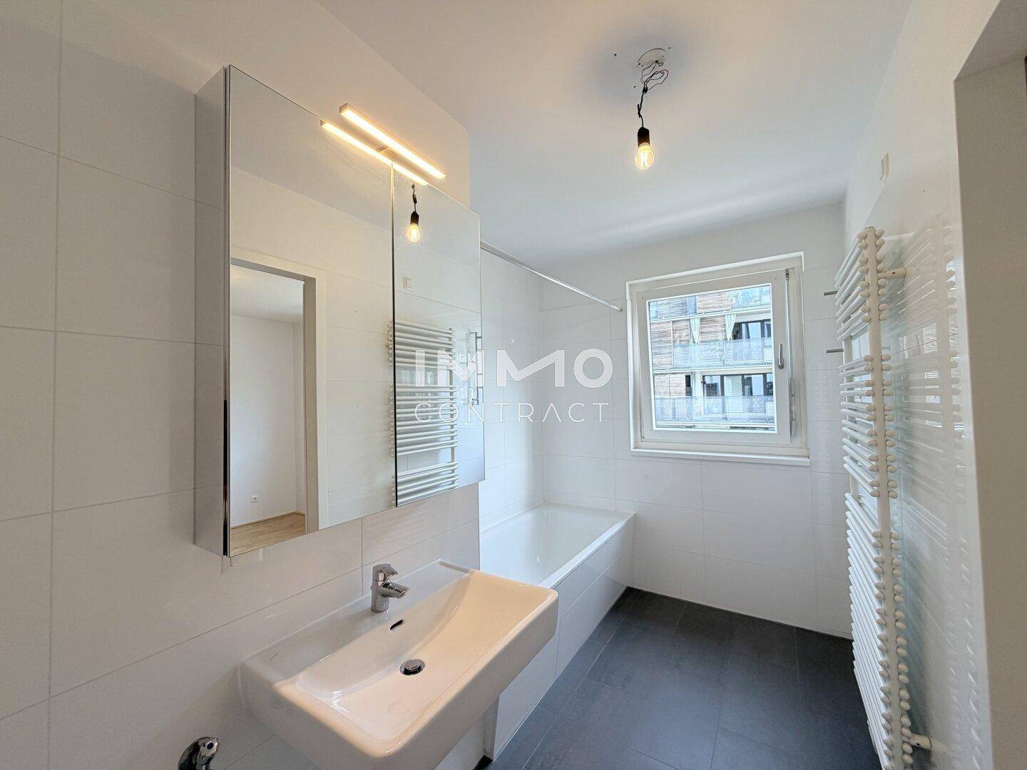 Helles Badezimmer mit Badewanne, Waschbecken, Spiegelschrank und beheiztem Handtuchhalter.