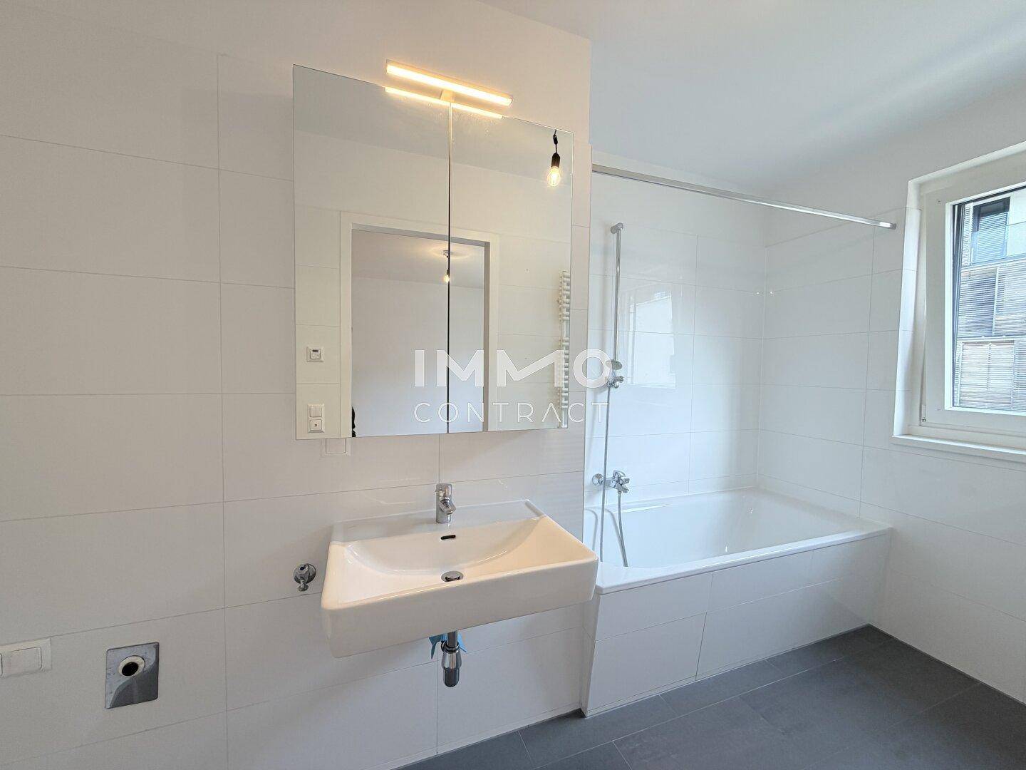 Modernes Badezimmer mit Badewanne, Waschbecken und großem Spiegel, hell gefliest.