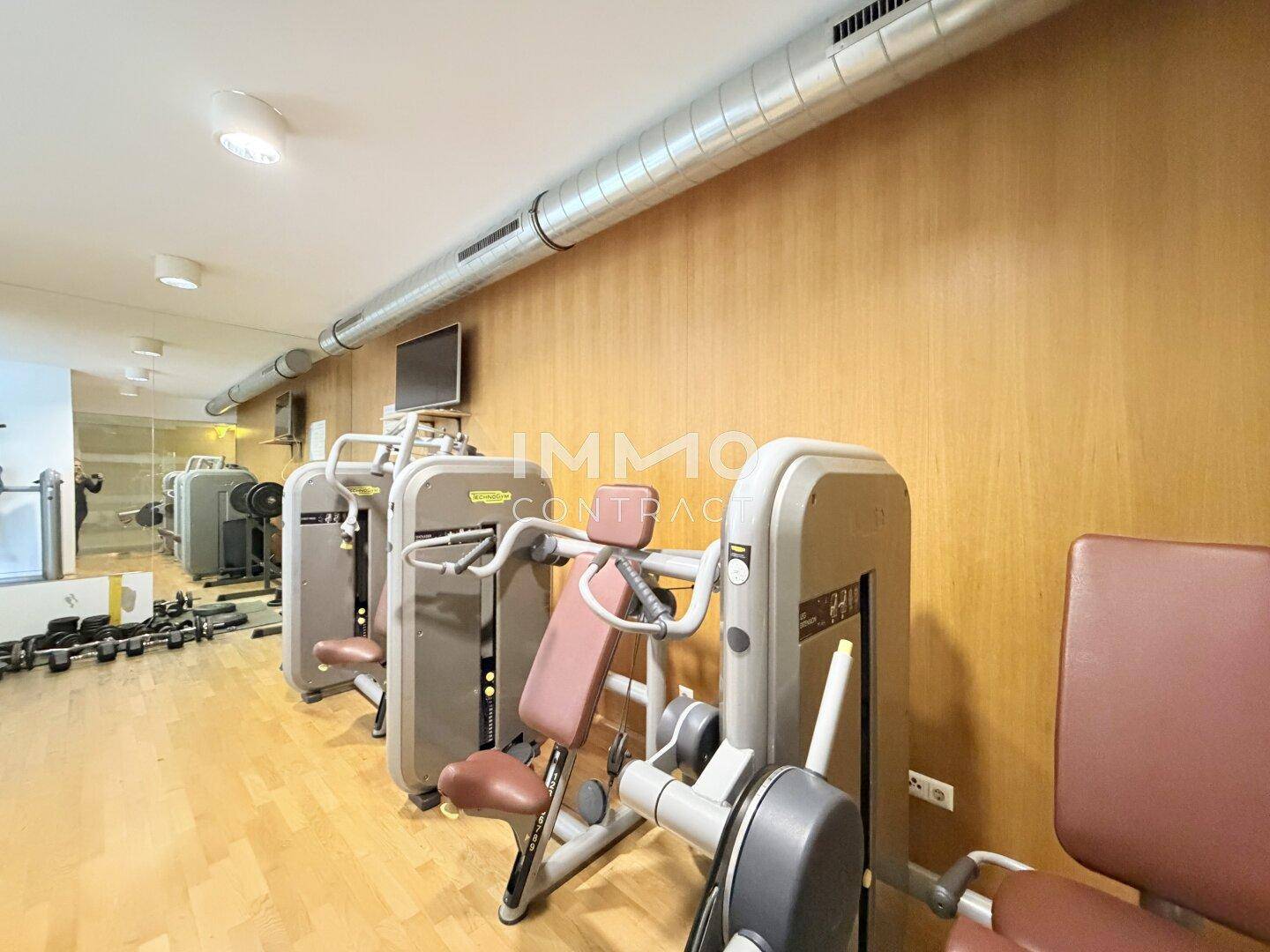 Moderner Fitnessraum mit verschiedenen Kraftgeräten und Holzverkleidung an den Wänden.