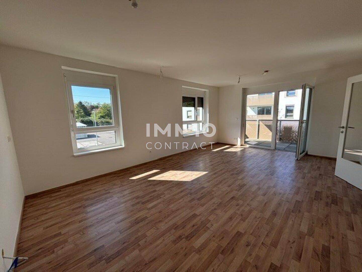 Helles Wohnzimmer mit Laminatboden, weißen Wänden und Zugang zu einem Balkon.