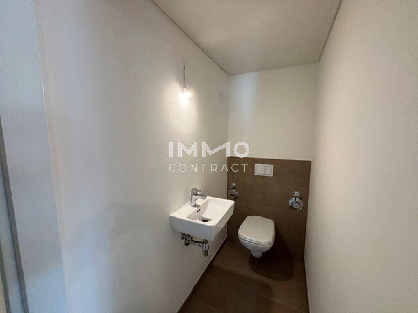 Gäste-WC mit wandhängender Toilette, kleinem Waschbecken und modernen Fliesen.