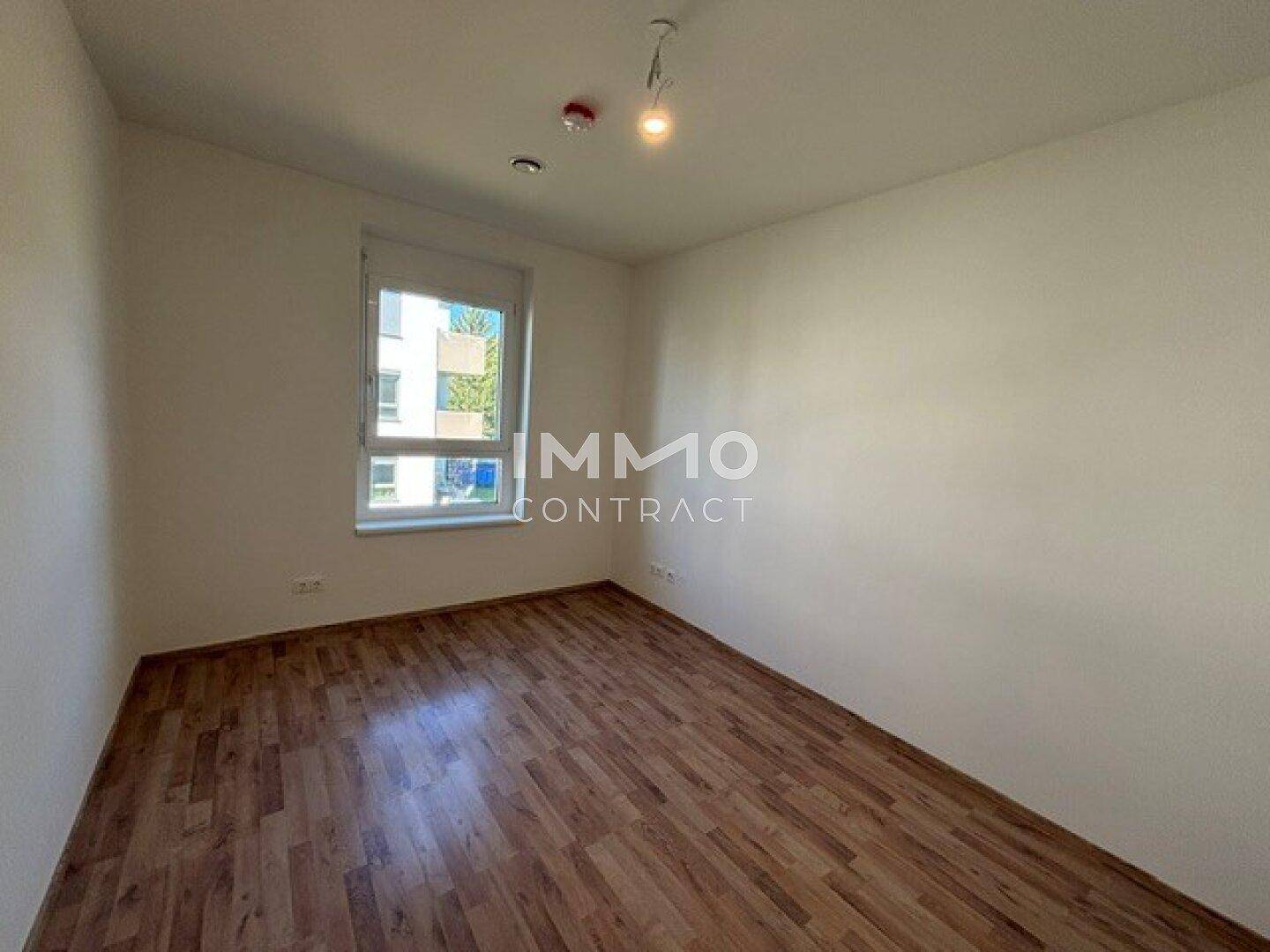 Helles Schlafzimmer mit Laminatboden, weißen Wänden und einem großen Fenster.