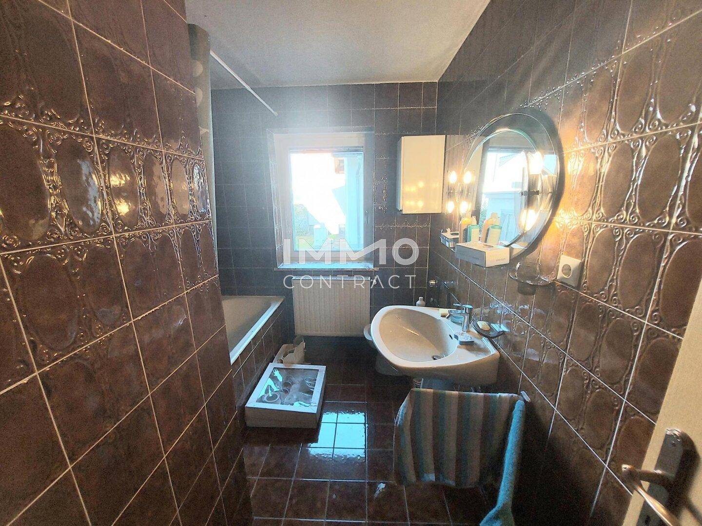 Badezimmer mit braunen Fliesen, Badewanne und Fenster für natürliche Belüftung.
