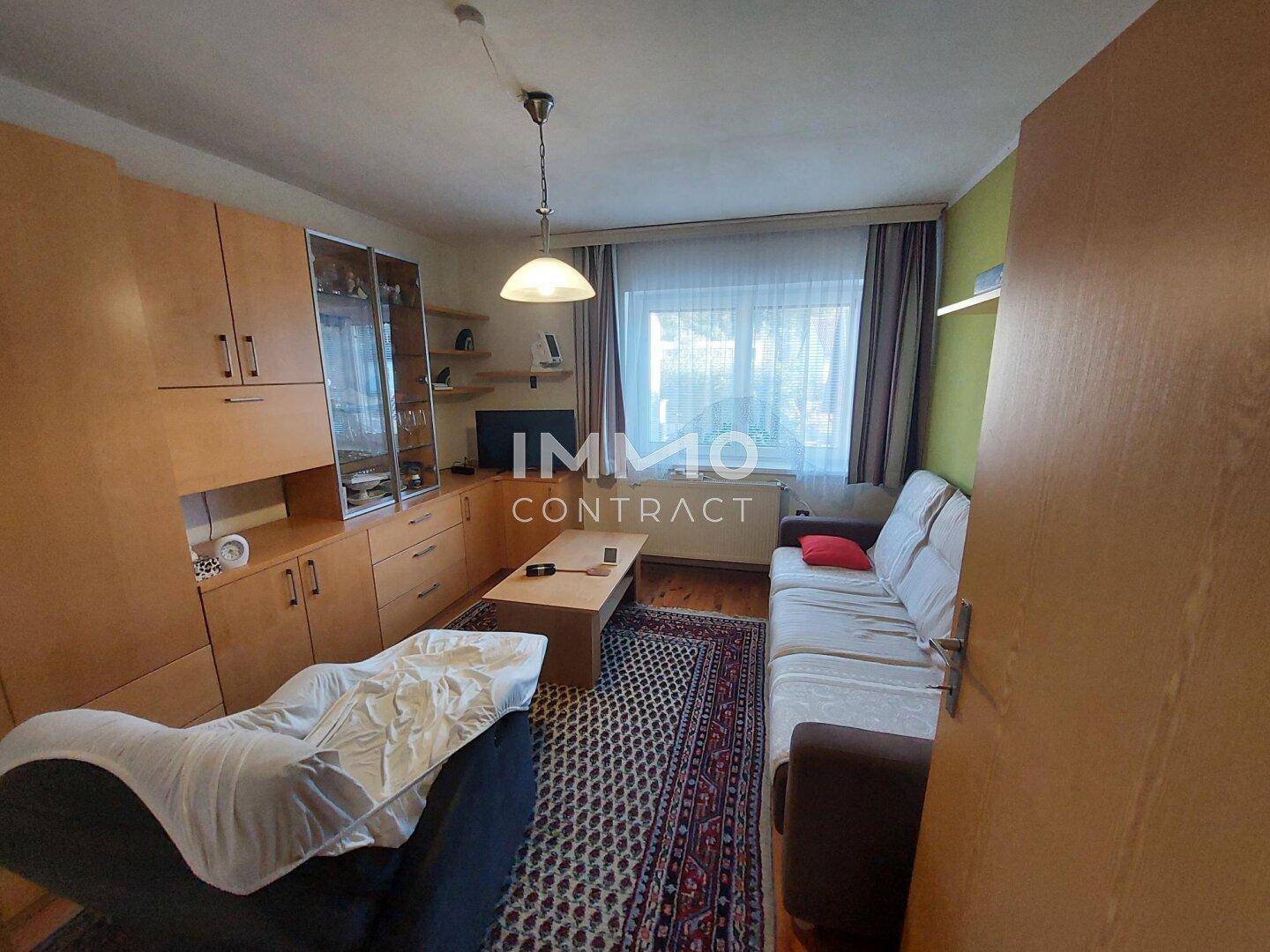 Wohnzimmer mit Holzmöbeln, Teppich und Fenster mit Blick nach draußen.