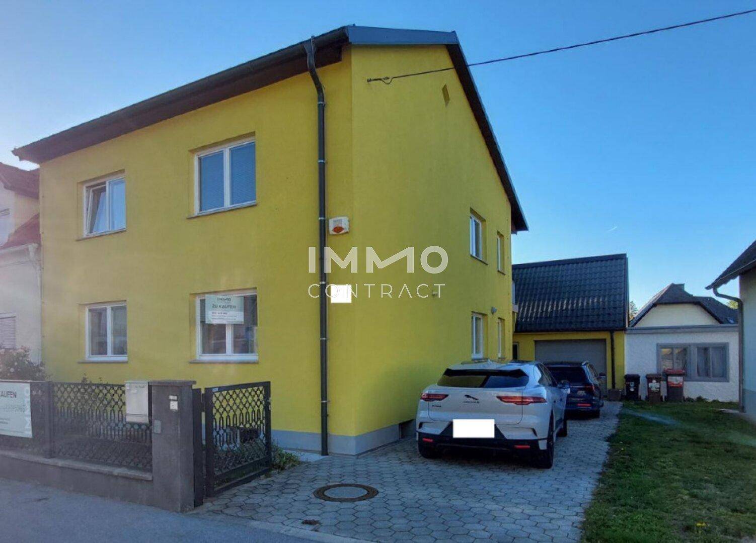 Gelbes Wohnhaus mit gepflasterter Einfahrt und Parkplätzen vor dem Gebäude.