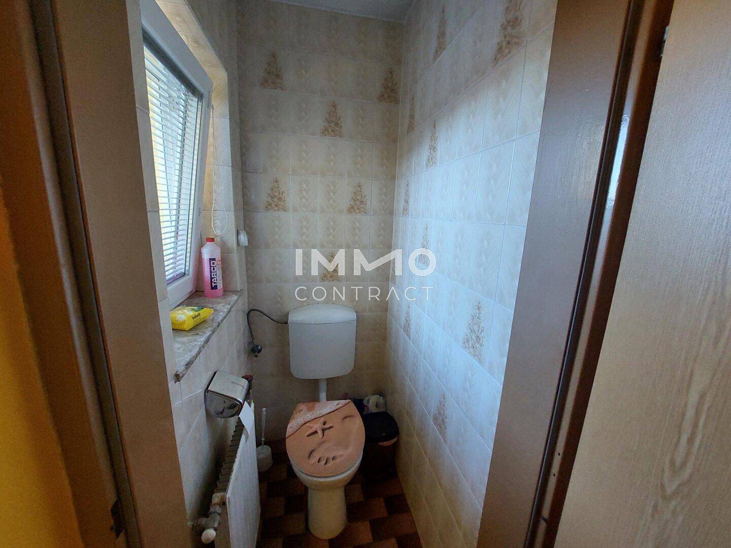 Kleines Gäste-WC mit Fenster, hellen Fliesen und einfacher Ausstattung.
