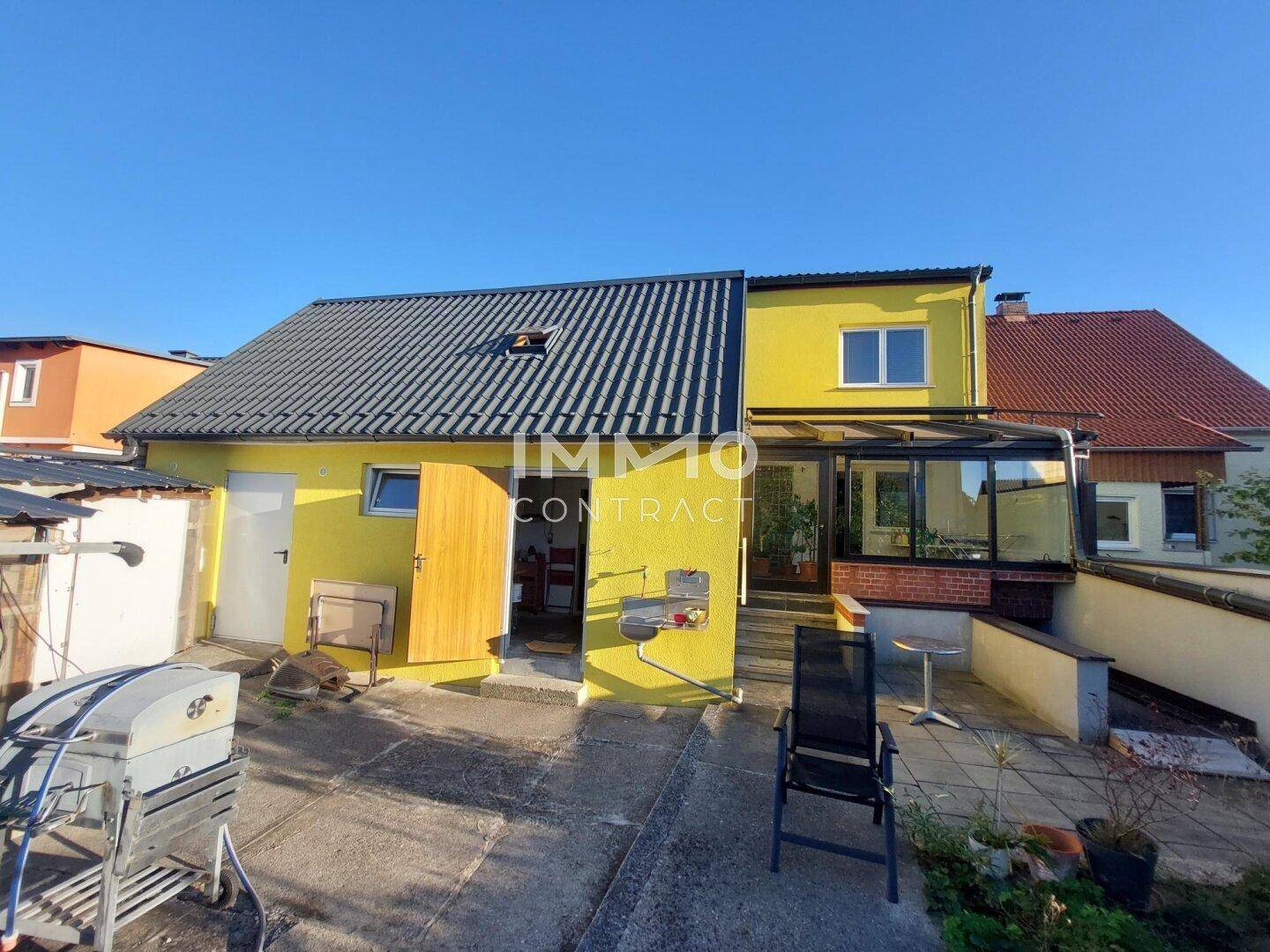 Hinterhof mit gepflasterter Terrasse, Grillbereich und einem Wintergarten am Haus.