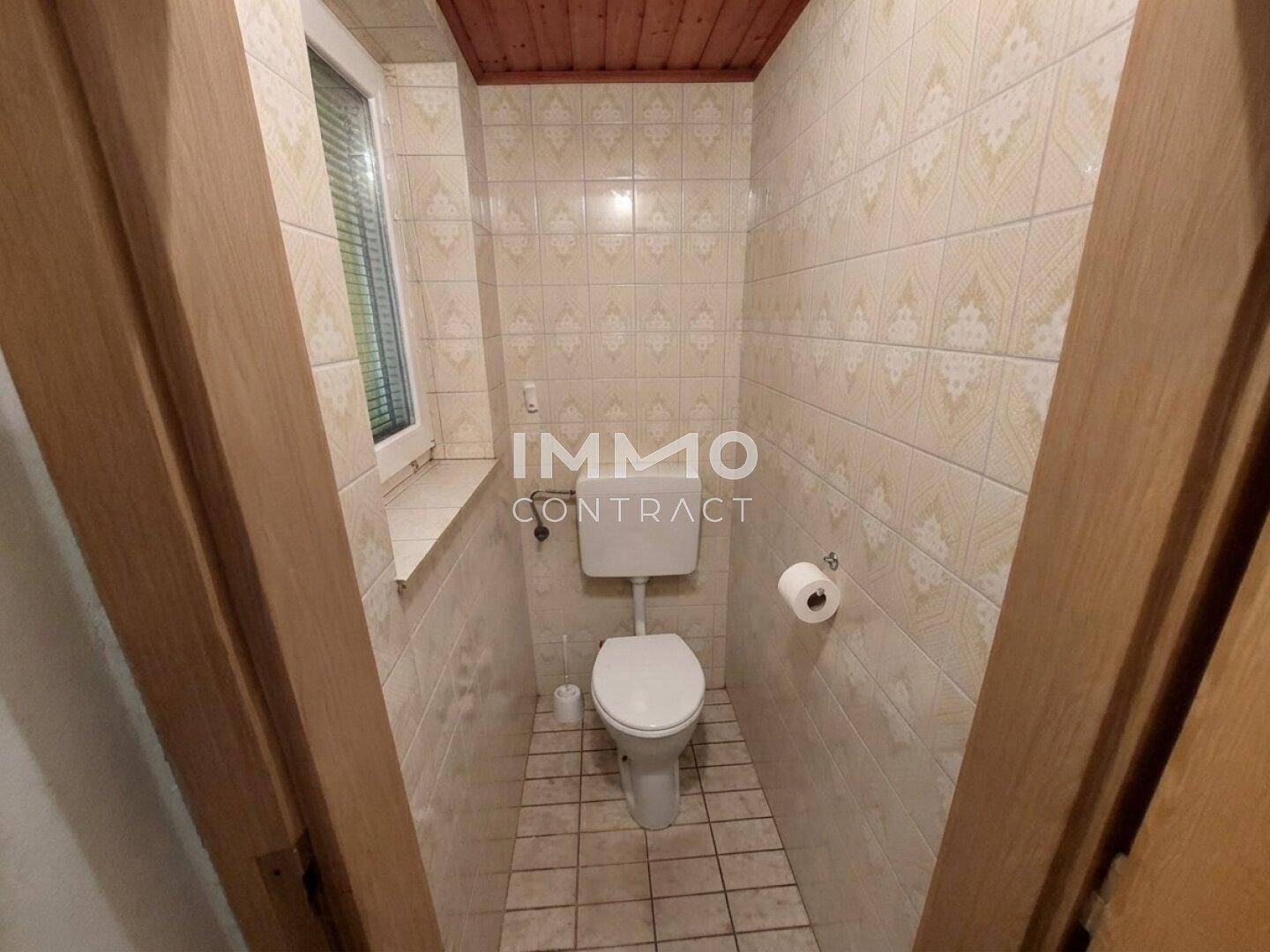 Separate Toilette mit hellen Fliesen, Fenster und einfacher Ausstattung.