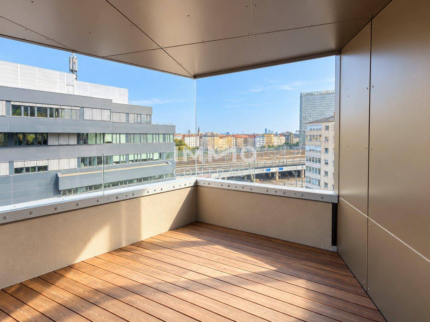 Geräumiger Balkon mit Holzboden und Glasgeländer, bietet einen weiten Blick über die Stadt und Umgebung.