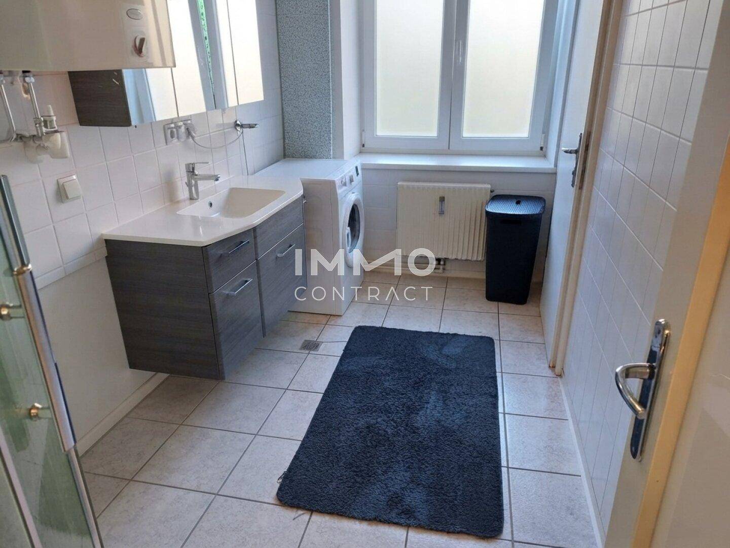 Funktionales Badezimmer mit Waschbecken, Toilette, Waschmaschine und Fenster für Tageslicht.