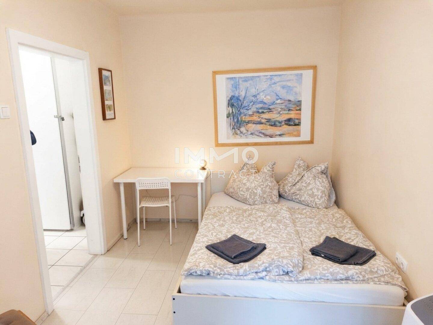 Kleines Schlafzimmer mit Einzelbett, Schreibtisch und hellem Fliesenboden.