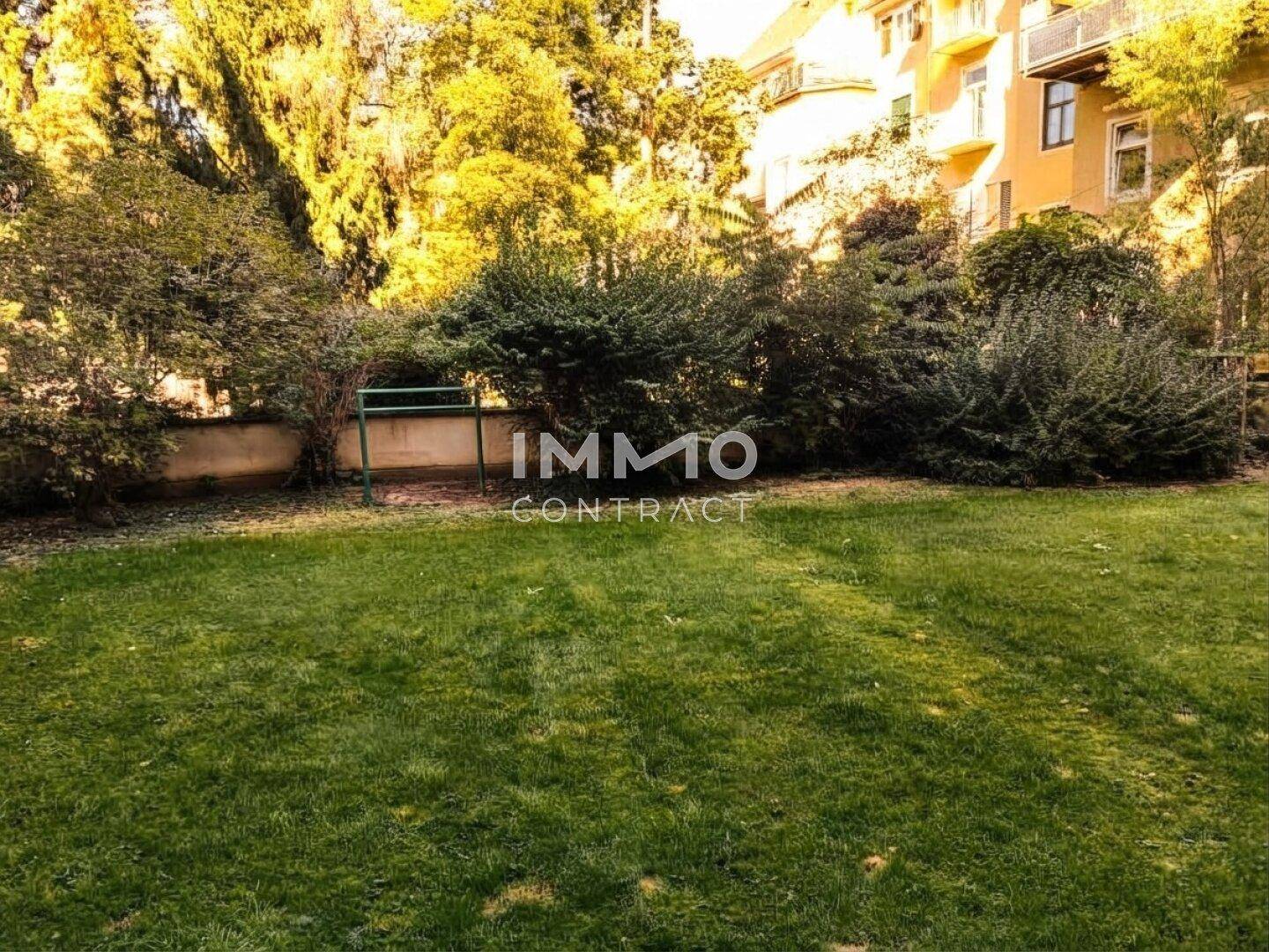 Gepflegter Gemeinschaftsgarten mit Rasenfläche und Sträuchern hinter dem Gebäude.
