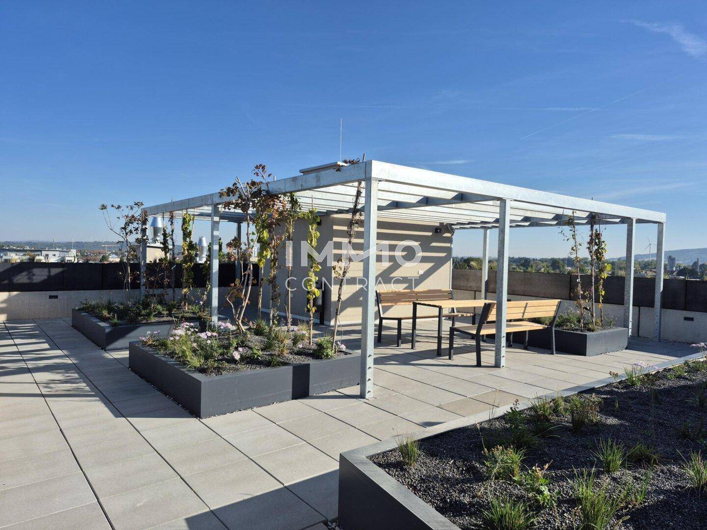 Großzügige Dachterrasse mit Pergola, Pflanzbeeten und Sitzgelegenheiten sowie Stadtblick.