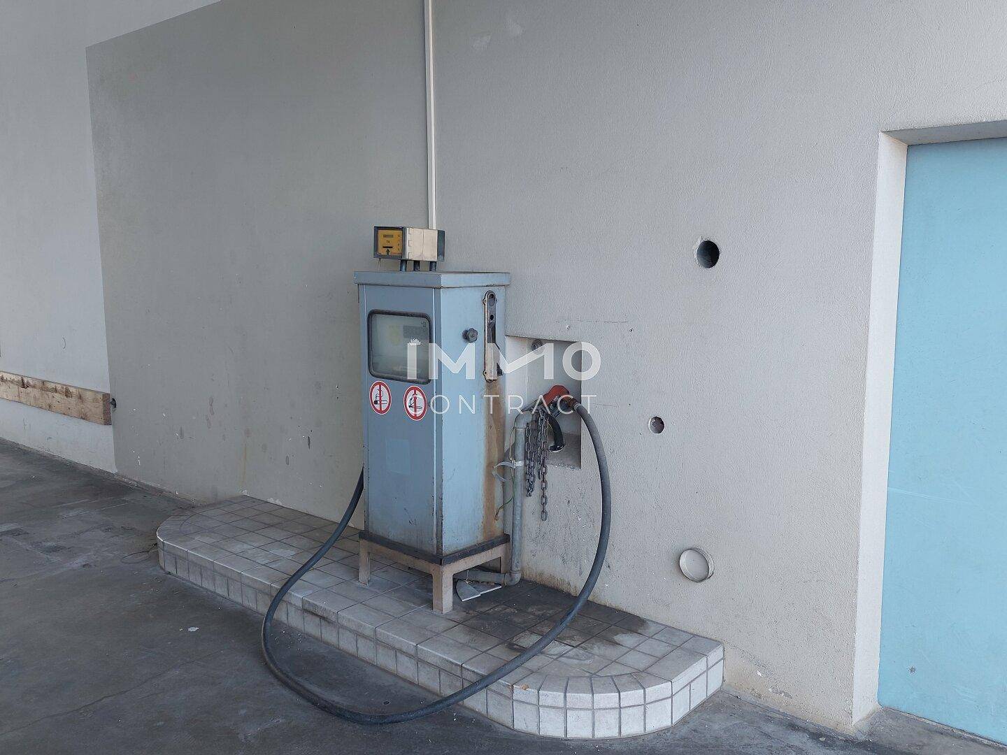 Industrielle Zapfsäule oder Pumpe auf gefliestem Podest neben einer Wand und einer blauen Tür.