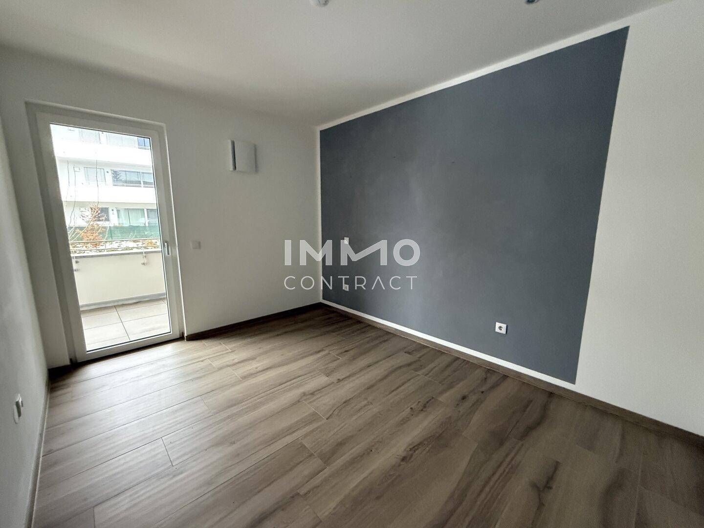 Schlafzimmer mit grauer Akzentwand, Holzboden und direktem Zugang zum Balkon.
