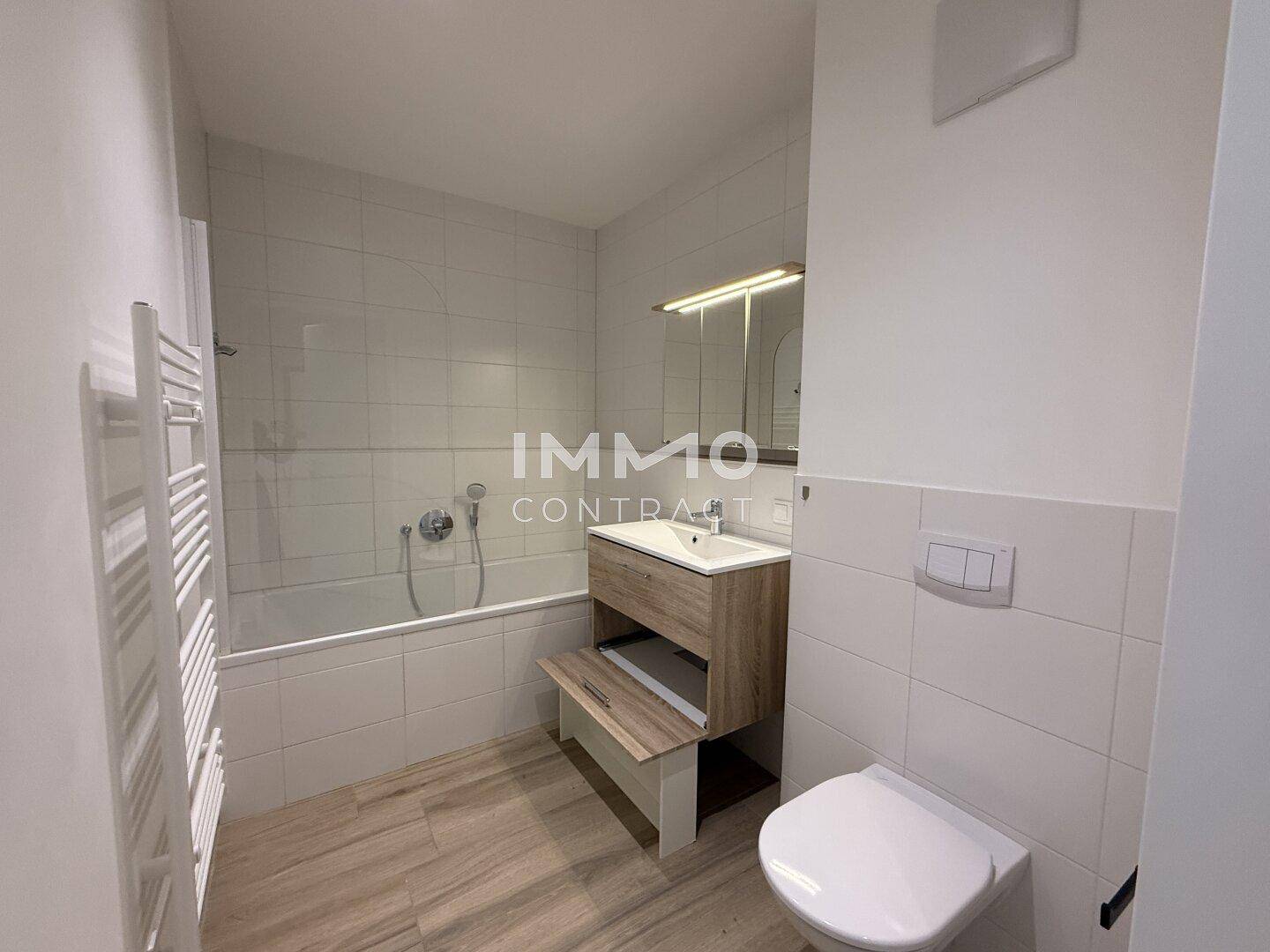 Modernes Badezimmer mit Badewanne, Waschtisch, WC und beheiztem Handtuchhalter.