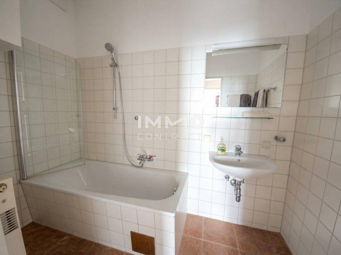 Helles Badezimmer mit Badewanne, Duschvorrichtung und weiß gefliesten Wänden.
