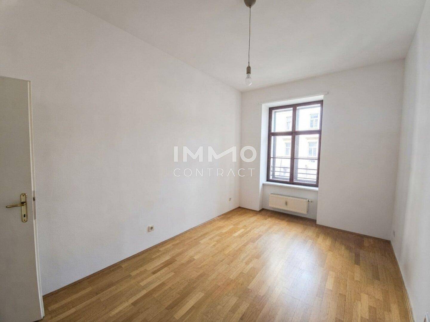 Heller Raum mit Holzboden und einem Fenster, das den Blick nach draußen freigibt.