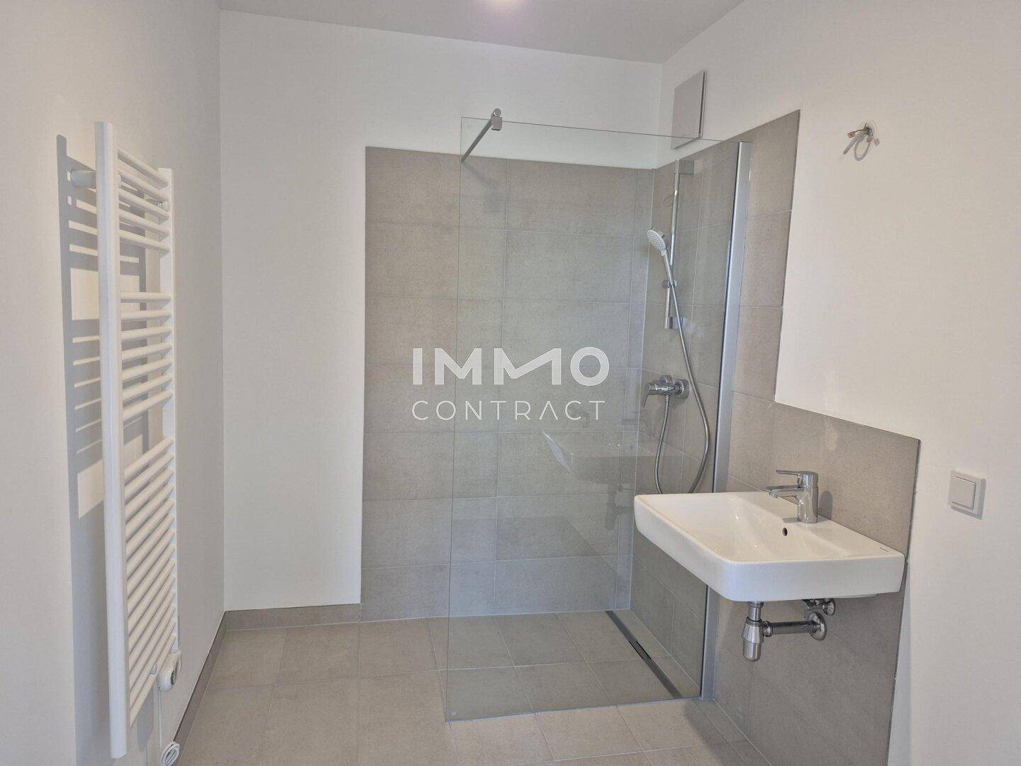 Modernes Badezimmer mit ebenerdiger Dusche, Einzelwaschbecken und beheiztem Handtuchhalter.