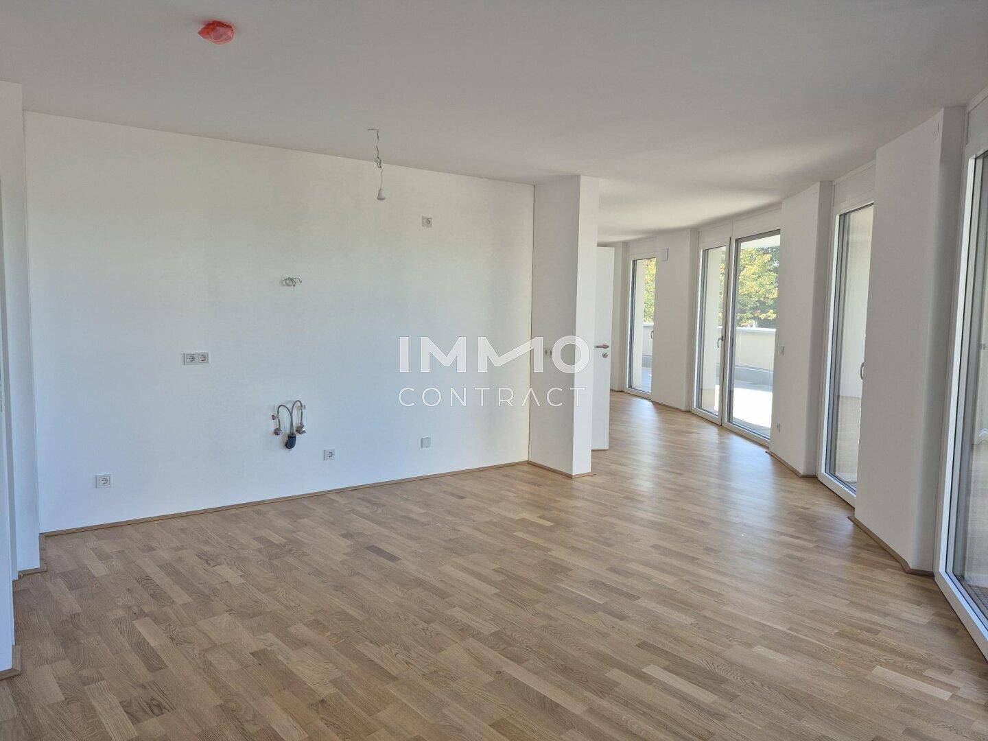 Geräumiger, heller Raum mit Holzboden und großen Fenstern, die viel Tageslicht hereinlassen.