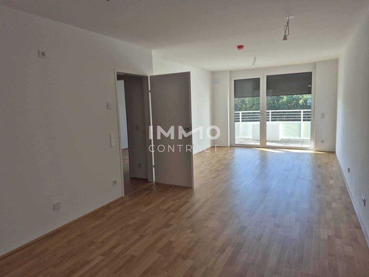 Geräumiges, helles Zimmer mit Parkettboden und Balkonzugang, ideal als Wohnbereich nutzbar.
